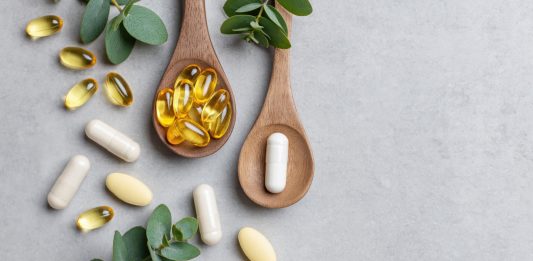 Omega-3-Kapseln und Nahrungsergänzungsmittel auf Holzlöffeln mit grünen Blättern auf hellem Hintergrund. Symbolbild für Fischöl, EPA, DHA, Omega-3-Präparate und Gesundheitsvorsorge.